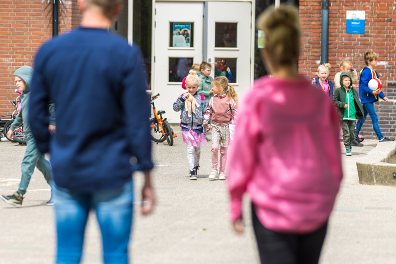 Twee ouders wachten op hun twee dochters op het schoolplein
