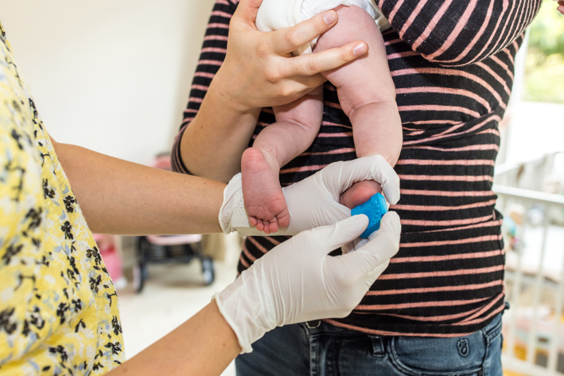 GGD Mederwerker Voert Staand De Hielprik Uit Bij Baby
