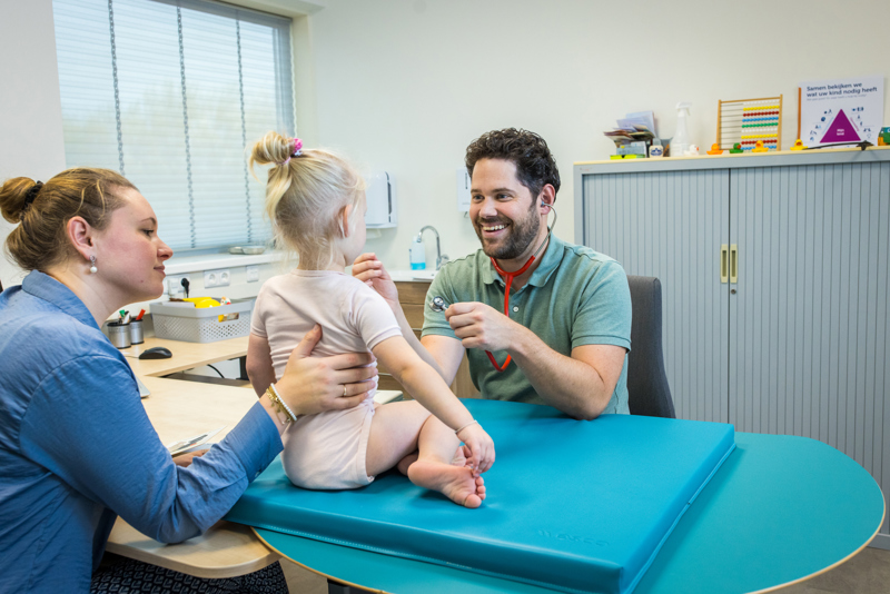 Jeugdarts Onderzoekt Lachend Kind En Moeder Houdt Haar Vast
